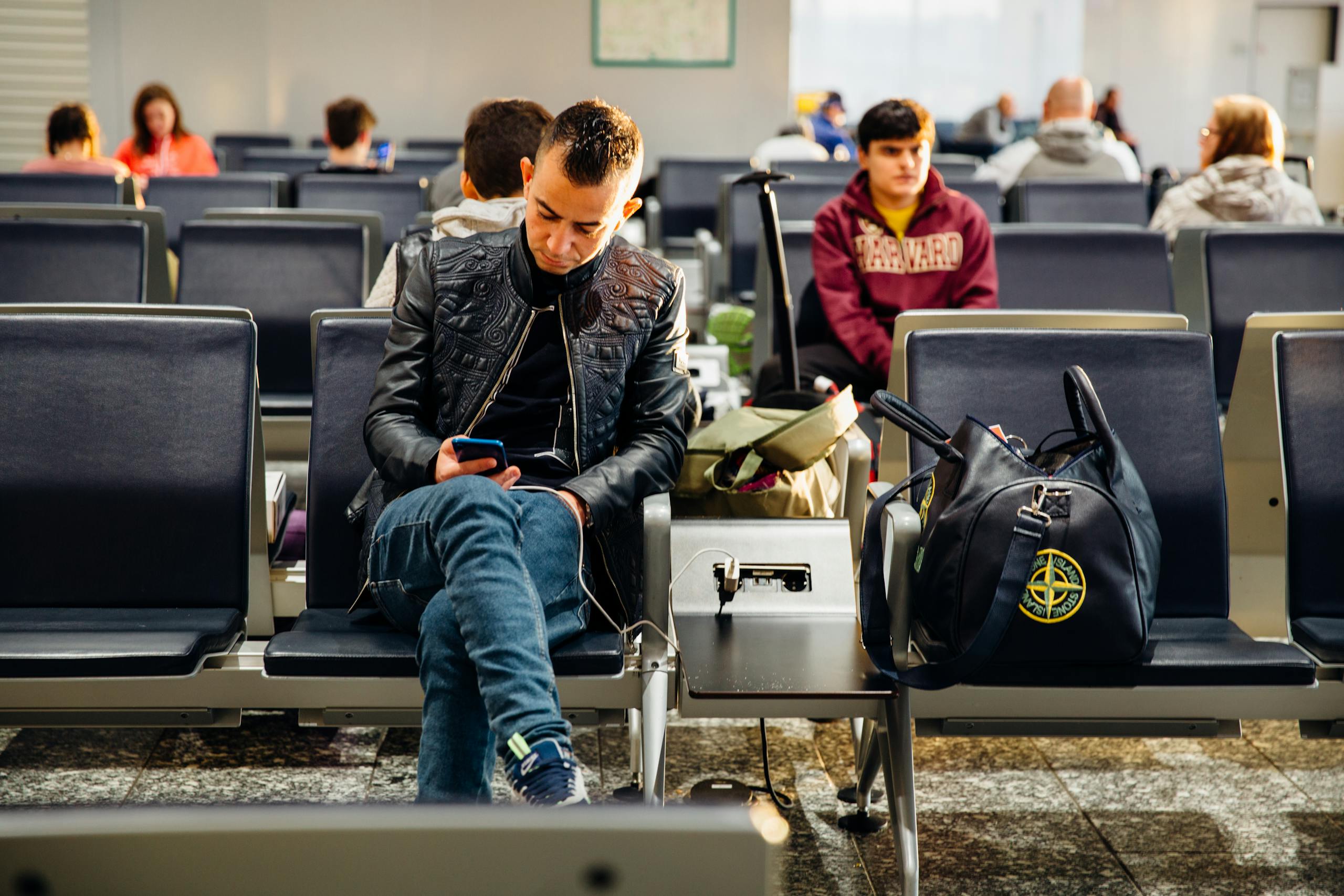 People sitting in an airport lounge, focused on smartphones and waiting for flights.