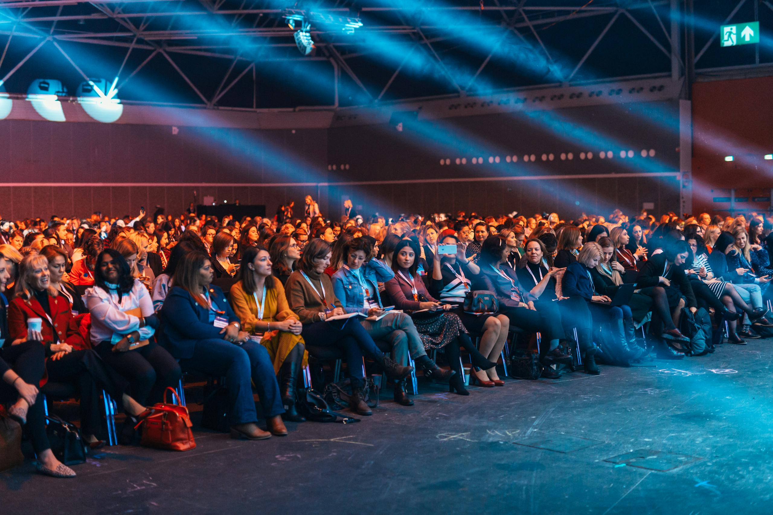 Vibrant image of a diverse audience seated in a large auditorium, highlighted by dynamic stage lighting.